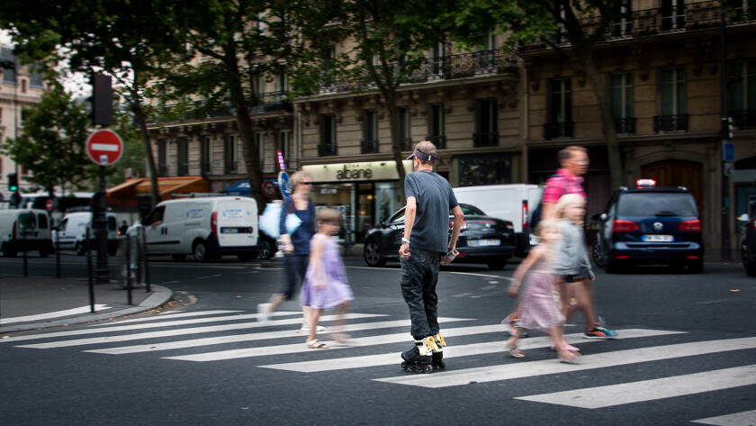A man roller skating over a zebra crossing in Paris, with a family walking behind going in the opposite direction.