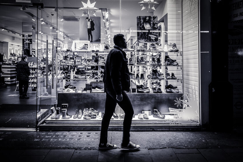 A man wearing Converse shoes walking past a shoe shop on Oxford Street at Christmas.