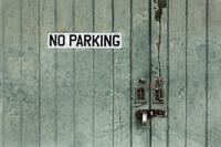 A padlocked garage door with peeling paint and No Parking sign.