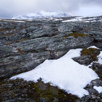 The last surviving snow from last year's snowfall, with rocks and a mountain in the background.